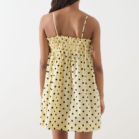 Model wearing Damson Madder Butter Spot Dress, back view, yellow cotton mini with black polka dots, shirred bodice and thin straps.