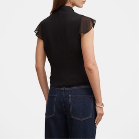 Model wearing black sleeveless top with sheer flutter sleeves, styled with dark blue wide-leg jeans and a gold cuff bracelet
