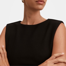 Model wearing black sleeveless top with bateau neckline, arms crossed, styled with gold stud earrings