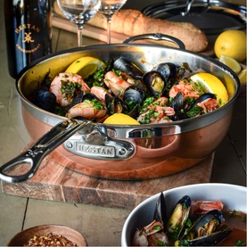 Hestan Copperbond Essential Pan 28cm in copper, filled with mussels, prawns and lemon, styled on a wooden board with wine and bread.
