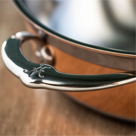 Hestan Copperbond Essential Pan 28cm close-up showing polished copper body, silver stainless steel helper handle and lid detail on wooden surface.