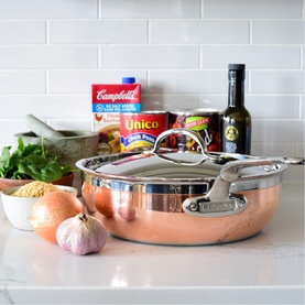 Hestan Copperbond Essential Pan with Helper Handle 28cm in copper, styled on a kitchen counter with cooking ingredients in the background.
