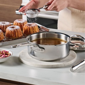 Hestan ProBond Luxe Covered Saucepan 18cm in stainless steel on marble trivet, with sauce inside, beside mini bundt cakes on cooling rack.