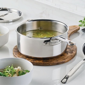 Hestan ProBond Luxe Covered Saucepan 22cm in polished stainless steel with helper handle, shown on wooden board with lid alongside bowls.