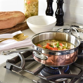 Hestan Copperbond Saucepan 18cm copper exterior with stainless steel handles, filled with vegetable soup, on a gas hob in a kitchen setting.