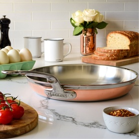 Hestan Copperbond Skillet 28cm in copper with stainless steel handle, styled on marble countertop with eggs, tomatoes and bread nearby.