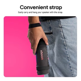 Libby xboom Grab by will.i.am Bluetooth Speaker in black with wrist strap, held in hand against pink background