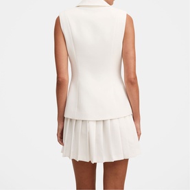 Model wearing white sleeveless blazer vest with notch lapel and double-breasted buttons, styled with matching white pleated mini skirt, rear view.