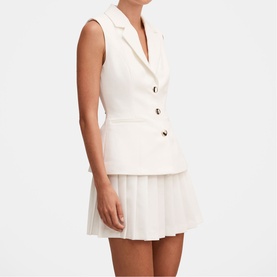 Model wearing cream sleeveless blazer vest with gold buttons, styled with matching pleated mini skirt