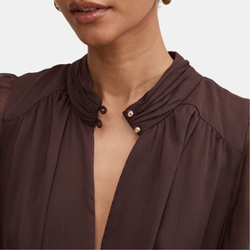 Model wearing dark brown sheer blouse with gathered neckline and gold button detail, styled close-up view