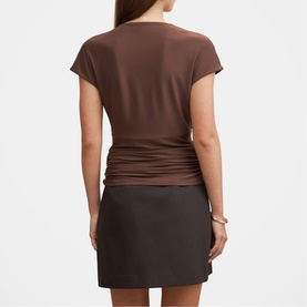 Model wearing brown short-sleeve ruched-back top with dark mini skirt, back view