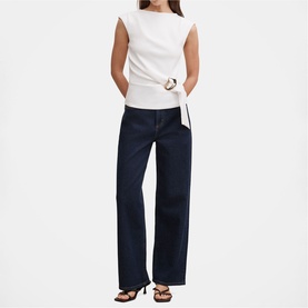 Model wearing white sleeveless wrap top with ring detail, styled with dark navy wide-leg jeans and brown sandals