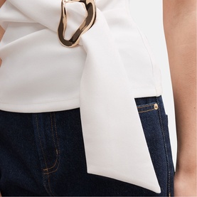 Model wearing white sleeveless top with gold ring bow detail, styled with dark indigo jeans