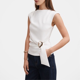 Model wearing white sleeveless top with gold D-ring belt detail, styled with dark navy trousers and gold bracelet