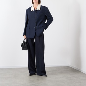 Model wearing navy blazer and wide-leg trousers with cream collar detail, carrying a small black bag, styled with black flat shoes