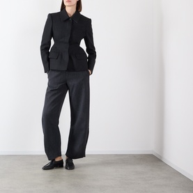 Model wearing black wool-blend blazer with structured shoulders and peplum waist, styled with wide-leg trousers and loafers
