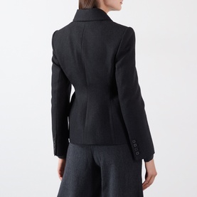 Model wearing black wool-blend blazer, rear view showing tailored fit, seam detailing and button cuffs, styled with grey wide-leg trousers