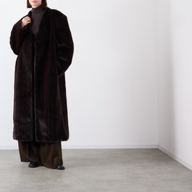 Model wearing Source Unknown Dhanila Faux Fur Coat in brown, longline with shawl collar, styled with wide-leg trousers and black shoes.