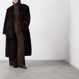 Model wearing Source Unknown Dhanila Faux Fur Coat in brown with shawl collar and longline silhouette, styled with wide-leg trousers and black flats