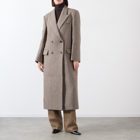 Model wearing Source Unknown Reyna Double-Breasted Coat in beige wool, peak lapel, longline fit, styled with brown trousers and black heels