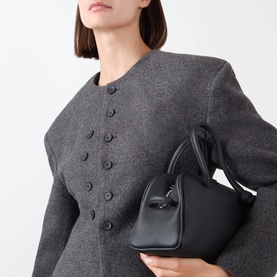 Model wearing Source Unknown Banton Double-Breasted Jacket in charcoal, collarless with structured shoulders, carrying a small black top-handle bag.