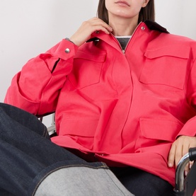 Model wearing Source Unknown Baia Fleece Field Jacket in red, styled with dark denim jeans. Snap button cuffs and front flap pockets visible.