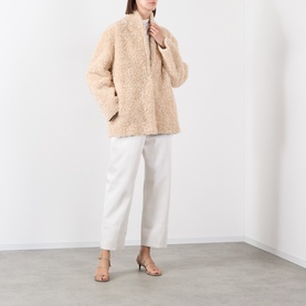Model wearing Source Unknown Manuela Shearling Jacket in beige with shawl collar, styled with white wide-leg trousers and nude heeled sandals.