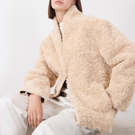 Model wearing Source Unknown Manuela Shearling Jacket in beige, faux shearling texture, funnel neck, styled with white trousers