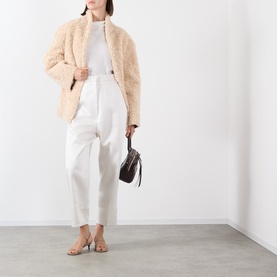 Model wearing Source Unknown Manuela Shearling Jacket in beige with white trousers and carrying a dark brown bag with nude heeled sandals.