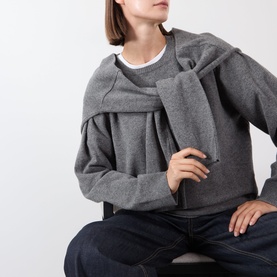 Model wearing Source Unknown Tio Shawl Sweater in charcoal, featuring draped shawl detail, round neck, and long sleeves, styled with navy jeans