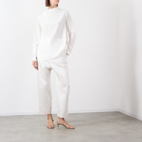 Model wearing Source Unknown Kuna Asymmetric Blouse in ivory with wide neckline and curved hem, styled with wide-leg cropped trousers and beige