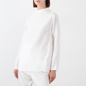 Model wearing Source Unknown Kuna Asymmetric Blouse in ivory with wide neckline, long sleeves and curved hem, styled with white trousers
