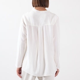 Model wearing Source Unknown Kuna Asymmetric Blouse in ivory, rear view showing box pleat detail, long sleeves and curved hem.