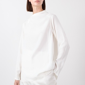 Model wearing Source Unknown Kuna Asymmetric Blouse in ivory, featuring wide neckline and long sleeves, styled with ivory trousers.