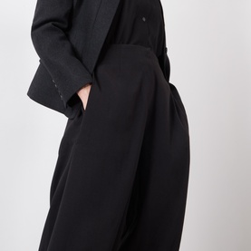 Model wearing Source Unknown Bimba Pintuck Trousers in black, wide-leg cropped silhouette with pintuck detailing, styled with a black blazer.
