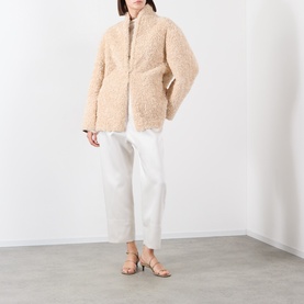Model wearing Source Unknown Ocelia Satin Trousers in white, cropped straight-leg fit, styled with a beige teddy fleece jacket and strappy heeled