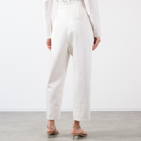 Model wearing Source Unknown Ocelia Satin Trousers in white, cropped straight-leg style, paired with nude strappy heeled sandals.