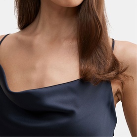 Model wearing navy satin slip dress with thin straps and draped cowl neckline, close-up detail shot