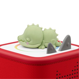 Tonies green sleeping dinosaur character figure resting on a red Toniebox speaker, with grey shark fin accessories nearby