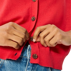 Model wearing Whistles red knit cardigan with dark horn buttons, styled with blue denim jeans. Close-up detail shot.
