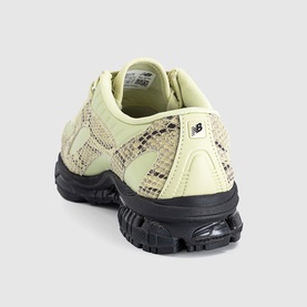 New Balance trainer in Morel Black with snake-effect panels, pale green leather upper, and chunky black rubber sole, rear view.