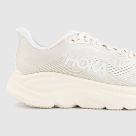 Hoka trainer in Alabaster Oat Milk, close-up showing embossed upper detailing, tonal laces, and chunky cream sole.