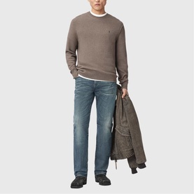 Model wearing taupe crew neck knit sweater and blue jeans, holding a jacket, styled with a white T-shirt and black shoes