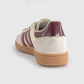 Adidas trainer in off-white suede with shadow red heel panel and three-stripe detail on gum rubber sole, rear angle view