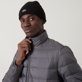 Model with Lacoste Croc Logo Rib-Knit Beanie Hat in black, ribbed construction with felt Croc logo, styled with a grey puffer jacket