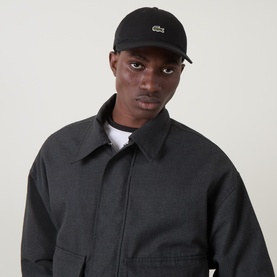 Model with Lacoste Croc Logo Baseball Cap in black, six-panel construction with embroidered croc logo, styled with dark zip-up jacket