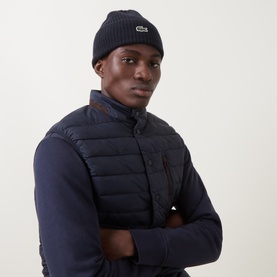 Model with Lacoste Croc Logo Rib-Knit Beanie Hat in navy blue, ribbed knit with felt Croc logo, styled with navy gilet and shirt