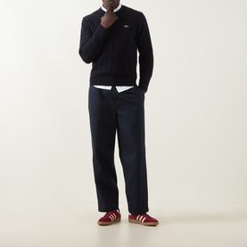 Model wearing Lacoste navy blue wool crew neck jumper, styled with white shirt, dark trousers and red trainers.