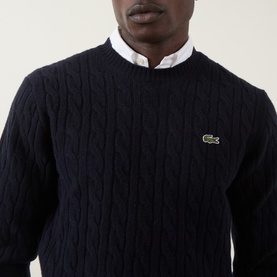 Model wearing Lacoste navy blue wool cable-knit crew neck jumper with signature crocodile logo, styled over a white collar shirt.