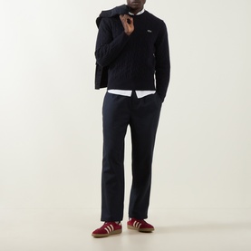 Model wearing Lacoste navy blue wool crew neck jumper, styled with white shirt, navy trousers and red trainers.